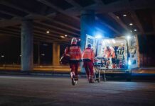 Paramedics load a stretcher into an ambulance at night under an overpass