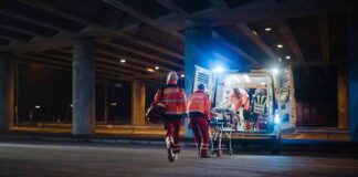 Paramedics load a stretcher into an ambulance at night under an overpass