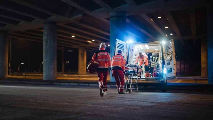 Paramedics load a stretcher into an ambulance at night under an overpass