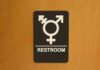 Restroom sign with gender-inclusive symbol on wooden door