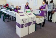 A Software Error Put Thousands Of Illegals On The Rolls Election workers near ballot boxes in a polling station