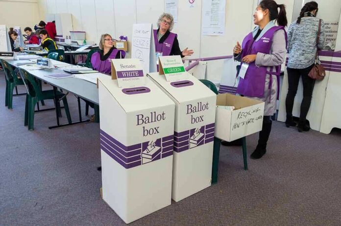 shutterstock_446230945 Election workers near ballot boxes in a polling station