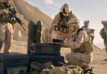 Soldiers in desert setting prepare equipment near rugged hills