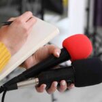 Mom Admits Smoking Meth Days Before Infant Died Journalist holding two microphones while writing in a notebook