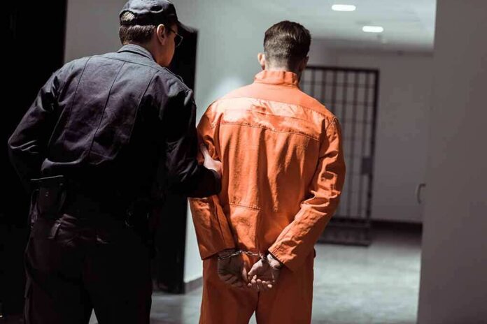 shutterstock_1030254055 Police officer escorting handcuffed inmate in orange jumpsuit