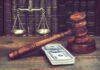 Judge's gavel beside cash and scales of justice on a wooden desk