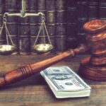 Judge's gavel beside cash and scales of justice on a wooden desk