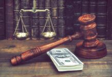 Judge's gavel beside cash and scales of justice on a wooden desk