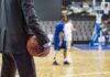 Courtside Chaos: Ban Follows Fiery Clash Basketball coach in suit holding ball courtside