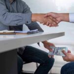 SPLC Poured Millions Into Extremist-Linked Informants Two people shake hands over a desk while cash is exchanged underneath