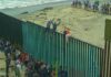 People climbing a tall beachside border fence