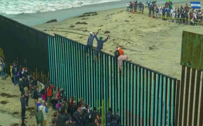People climbing a tall beachside border fence