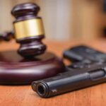 Gavel beside a handgun on a wooden table