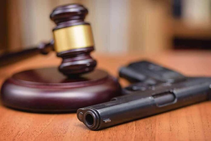 shutterstock_1329218465 Gavel beside a handgun on a wooden table