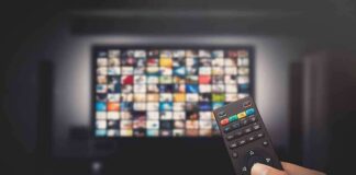 Hand holding TV remote toward a screen with streaming thumbnails