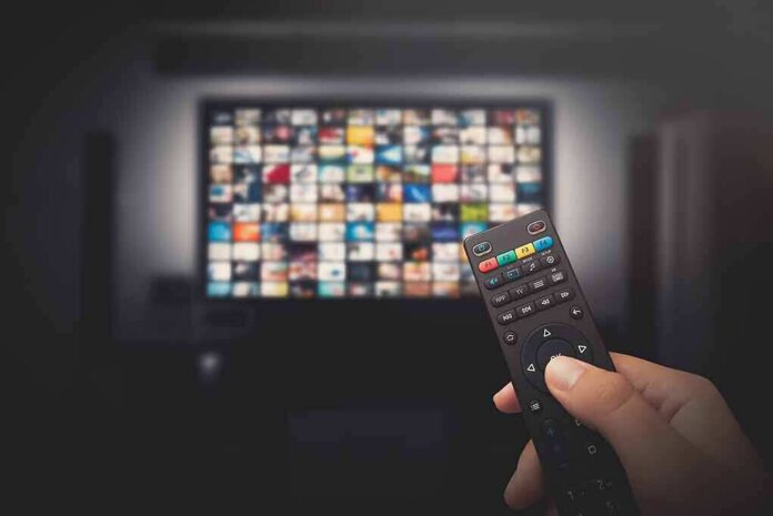 Hand holding TV remote toward a screen with streaming thumbnails