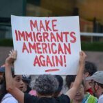 Teddy Williams at a protest holding a sign reading 'Make Immigrants American Again'
