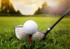 A golf ball on a tee with a golf club resting beside it on green grass