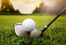 A golf ball on a tee with a golf club resting beside it on green grass