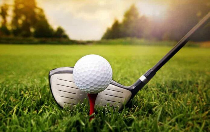 A golf ball on a tee with a golf club resting beside it on green grass