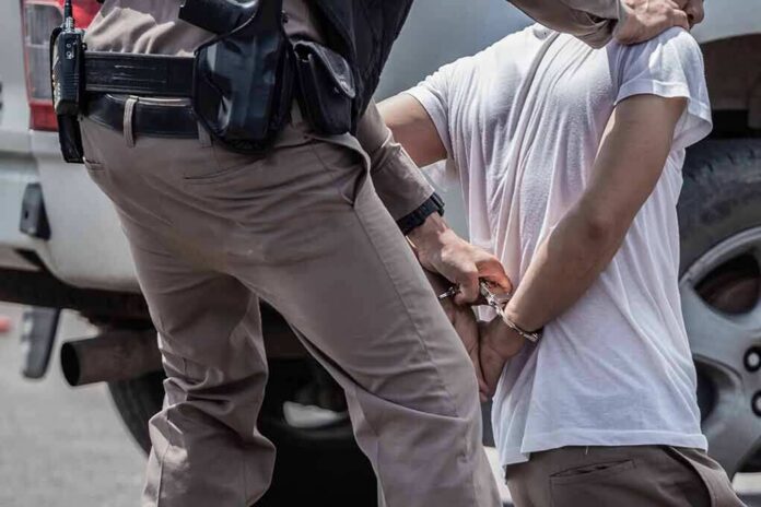 police officer handcuffing a person beside a vehicle