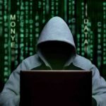 Hooded figure using a laptop against green code backdrop
