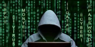 Hooded figure using a laptop against green code backdrop