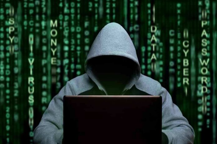 Hooded figure using a laptop against green code backdrop