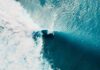 Surfer riding a large turquoise wave from above