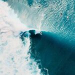 Surfer riding a large turquoise wave from above