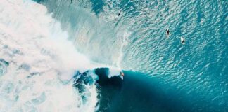 Surfer riding a large turquoise wave from above