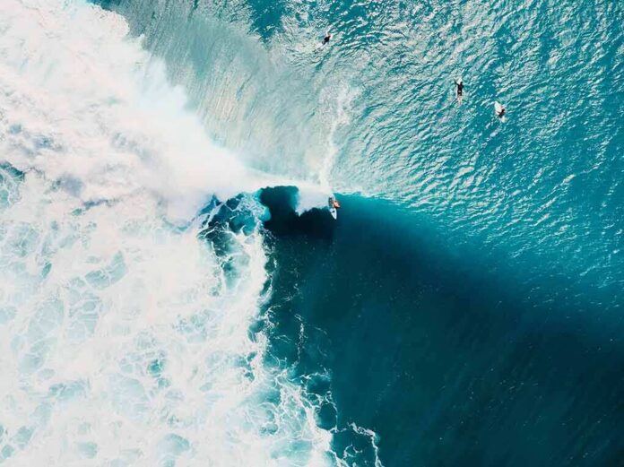 Surfer riding a large turquoise wave from above