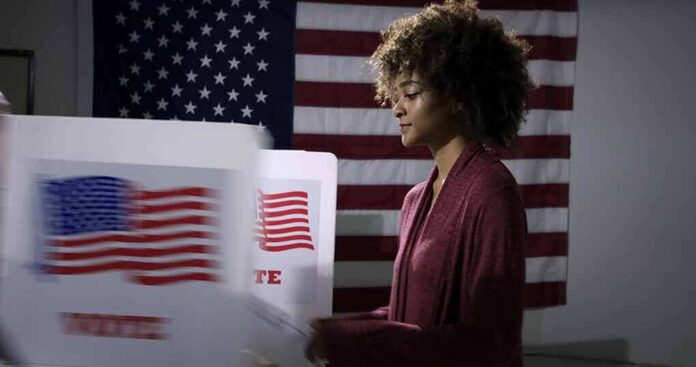 shutterstock_1737374753 Voter at a polling booth with an American flag backdrop