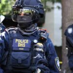 ICE Plans to Arm Agents With Electric Shock Gloves Riot police officer in tactical gear with helmet and visor