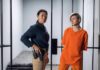 Police officer stands beside inmate in orange uniform inside a jail cell