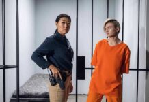 Police officer stands beside inmate in orange uniform inside a jail cell