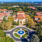 Aerial view of a campus building with red-tile roofs and a round fountain plaza