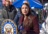 Woman speaking at outdoor press event with microphone and seal