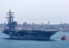 Aircraft carrier escorted by a tugboat in a harbor