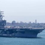 Aircraft carrier escorted by a tugboat in a harbor