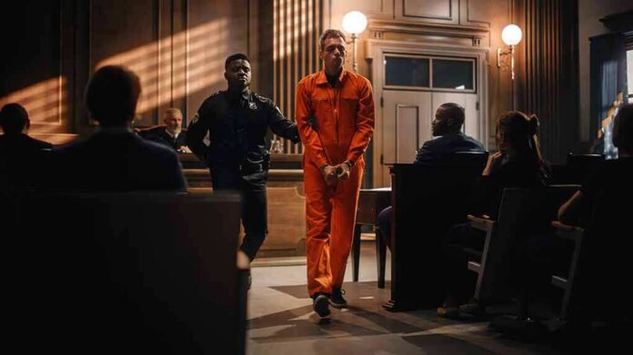 Defendant in orange jumpsuit escorted by officer in courtroom