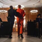 Prisoner in orange jumpsuit escorted by officer in a courtroom