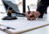 Why Is Clancy’s Lawyer Asking Trump for a Pardon? Hand signing legal document beside gavel and laptop
