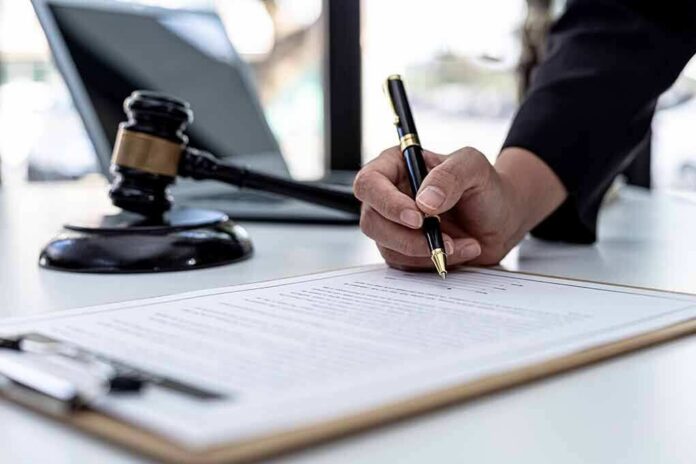 Hand signing legal document beside gavel and laptop