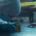 forensic investigator in protective suit examining crime scene markers