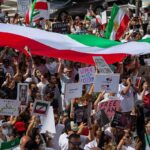 Protest crowd with flags and signs; Seyed Ebrahim Raisi, La Parka, Brian Robiskie, Philly Brown, Miguel Francisco Barragán Andrade present