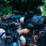 AI Backfires, Ford Rushes In Veterans TV news cameras crowding together at an outdoor event
