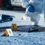 Forensic investigator examines a crime scene with evidence markers and a handgun