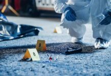 Forensic investigator examines a crime scene with evidence markers and a handgun