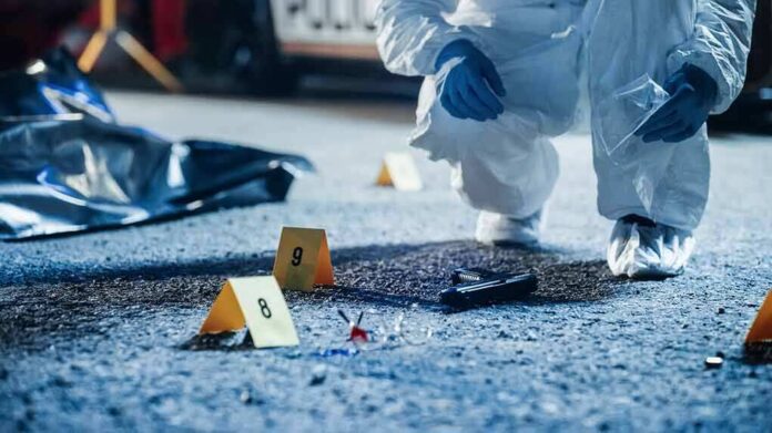 Forensic investigator examines a crime scene with evidence markers and a handgun